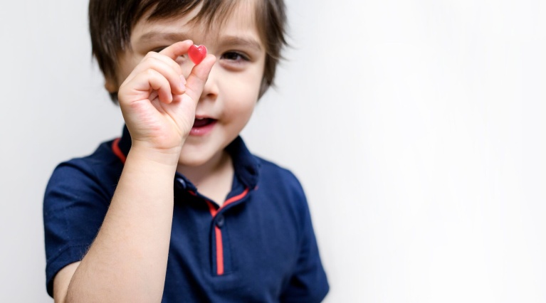 Kind in blauem Hemd hält ein kleines rotes Herzsymbol zwischen Daumen und Zeigefinger.