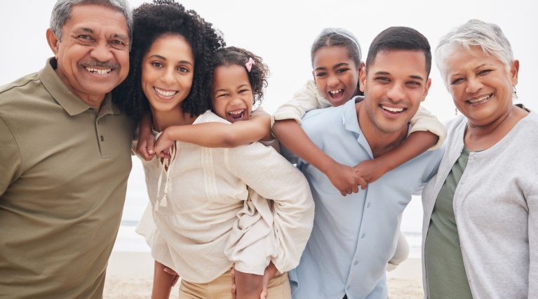 Mehrgenerationenfamilie lächelt gemeinsam am Strand, zeigt Lebensfreude und Zusammenhalt.