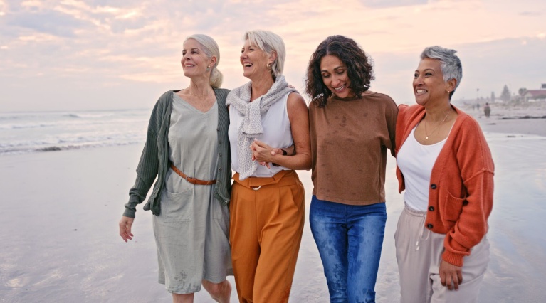 Frauen mittleren Alters spazieren am Strand und umarmen sich bei Sonnenuntergang.