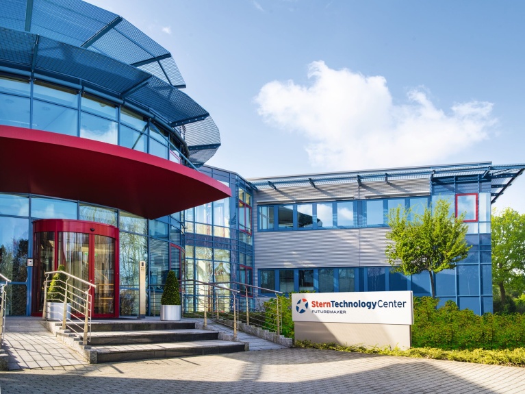 Eingang des Stern Technology Centers mit Glasfassade und roter Überdachung, umgeben von Pflanzen.