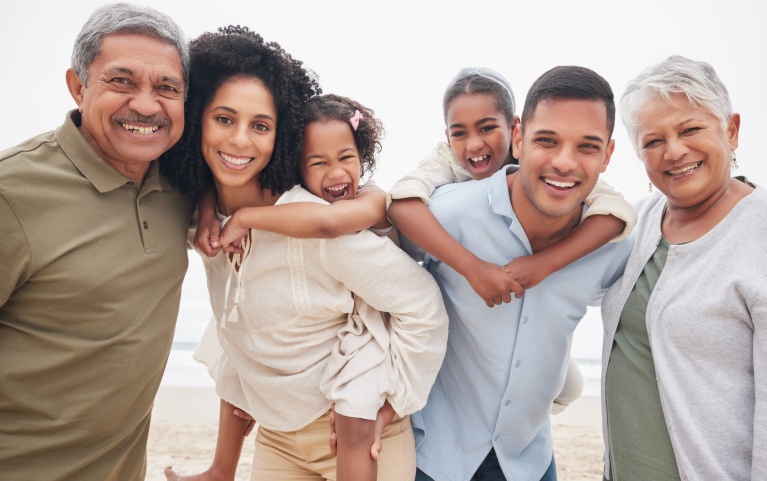Mehrgenerationenfamilie lächelt gemeinsam am Strand, zeigt Lebensfreude und Zusammenhalt.