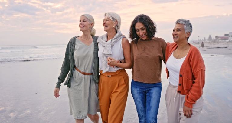 Frauen mittleren Alters spazieren am Strand und umarmen sich bei Sonnenuntergang.