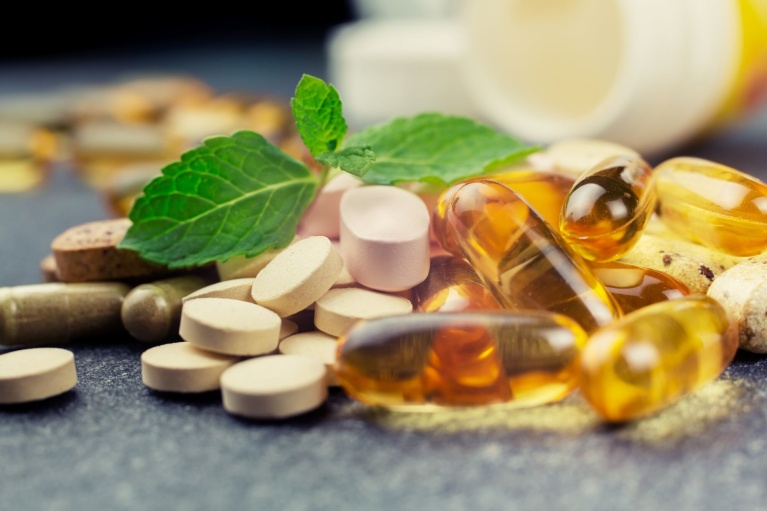 Verschiedene Nahrungsergänzungsmittel in Tabletten- und Kapselform mit einem frischen grünen Blatt.