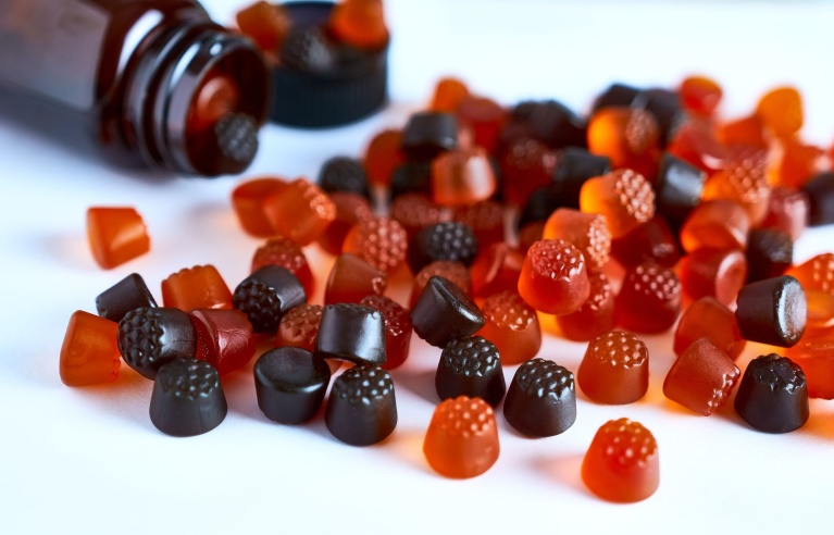 Verschiedene Gummibonbons zerstreut auf weißer Fläche, aus umgefallener Braunglasflasche.