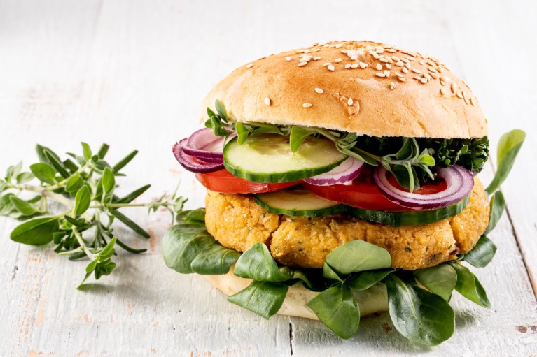 Vegetarischer Burger mit Kichererbsen-Patty, Tomaten, Gurken, Rotzwiebeln, Salat und Sesambrötchen.