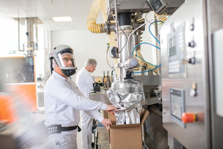 Mitarbeiter in Schutzkleidung überwachen Abfüllung von Mikronährstoffpremixen in Produktionshalle.