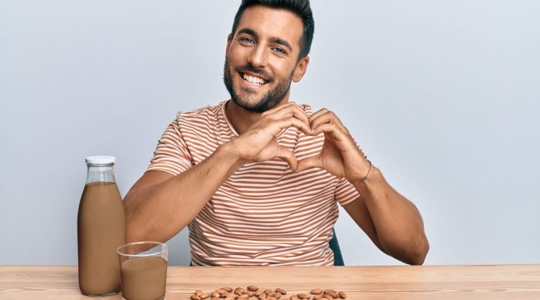 Mann zeigt Herz-Geste an Tisch mit Mandeln, Glas und Flasche Schokoladenmilch.