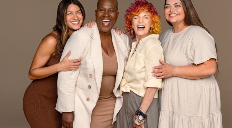 Vier Frauen unterschiedlichen Alters und ethischer Herkunft lachend und eng beieinander.