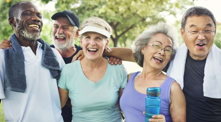 Fünf lachende Senioren nach dem Sport im Park, eine Frau hält eine Trinkflasche.