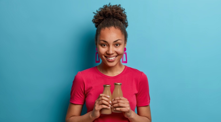 Afrikanische Frau im pinken Shirt präsentiert zwei Schokoladengetränke vor blauem Hintergrund.