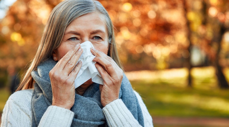 Ältere Frau putzt sich die Nase im Park. 