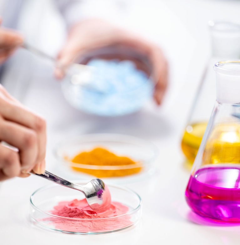 Laborant untersucht farbiges Mikronährstoff-Pulver aus einer Petrischale neben Erlenmeyerkolben.
