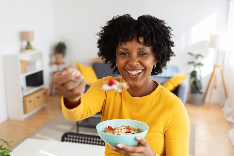 Lächelnde Frau hält eine Schüssel mit Müsli und Beeren direkt in die Kamera.