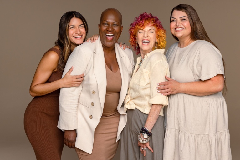 Vier Frauen unterschiedlichen Alters und ethischer Herkunft lachend und eng beieinander.
