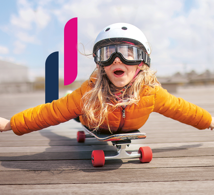 Lachendes Mädchen mit Helm und Brille „fliegt“ auf einem Skateboard.