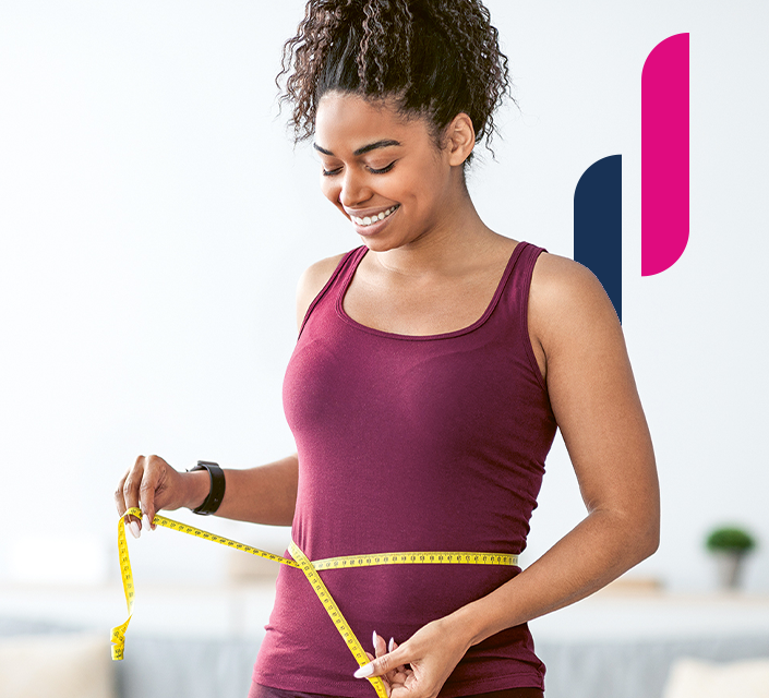 Lächelnde Frau in Sportkleidung misst ihren Taillenumfang mit einem Maßband.