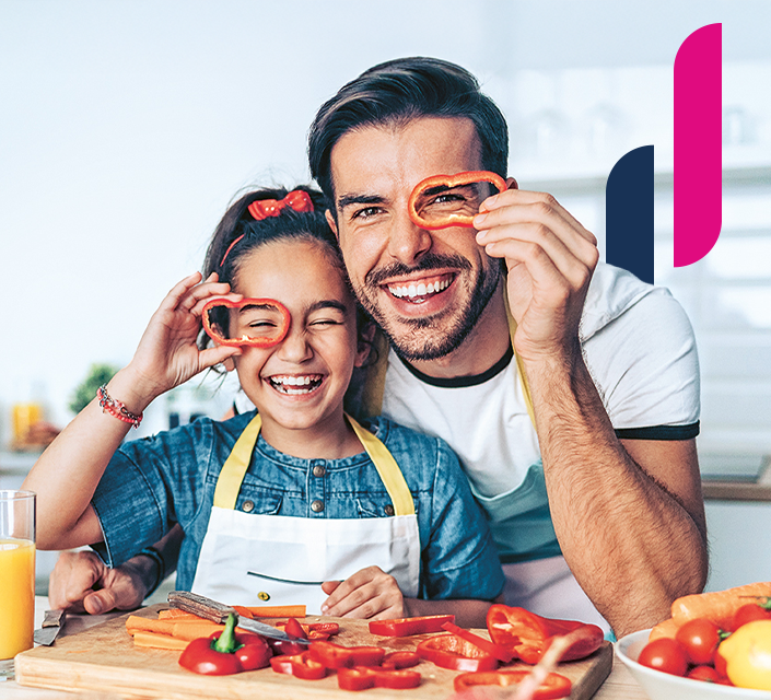 Lachender Vater und Tochter halten sich Paprikaringe wie Brillen vor die Augen.