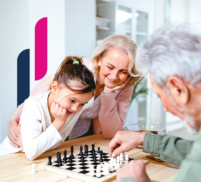 Zwei Erwachsene schauen einem Kind beim Schachspielen am Tisch zu.