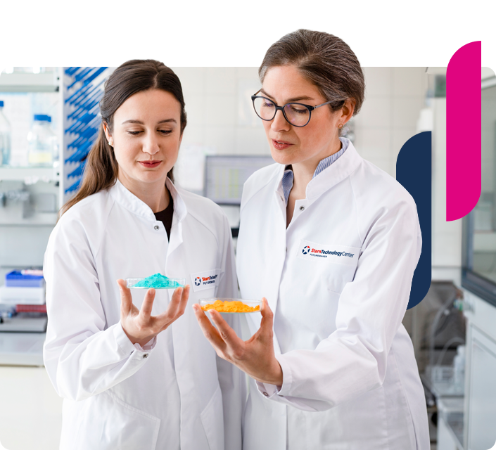 Zwei Personen stehen mit Kitteln im Labor und schauen auf farbige Mikronährstoffpulver. 