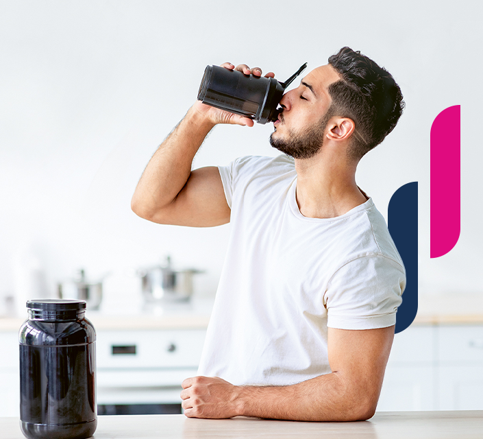 Sportler trinkt Protein-Shake aus Shaker, schwarze Dose steht daneben auf einem Tisch.