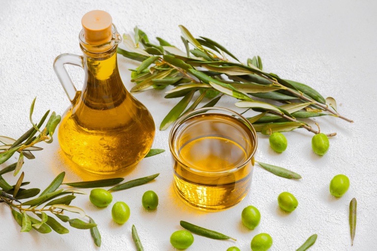 Goldenes Olivenöl in einer Karaffe und Schale neben frischen Olivenzweigen.