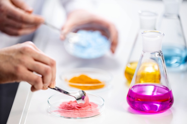 Laborant untersucht farbiges Mikronährstoff-Pulver aus einer Petrischale neben Erlenmeyerkolben.