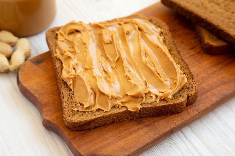 Vollkorntoast mit cremiger Erdnussbutter bestrichen auf einem Holzbrett.