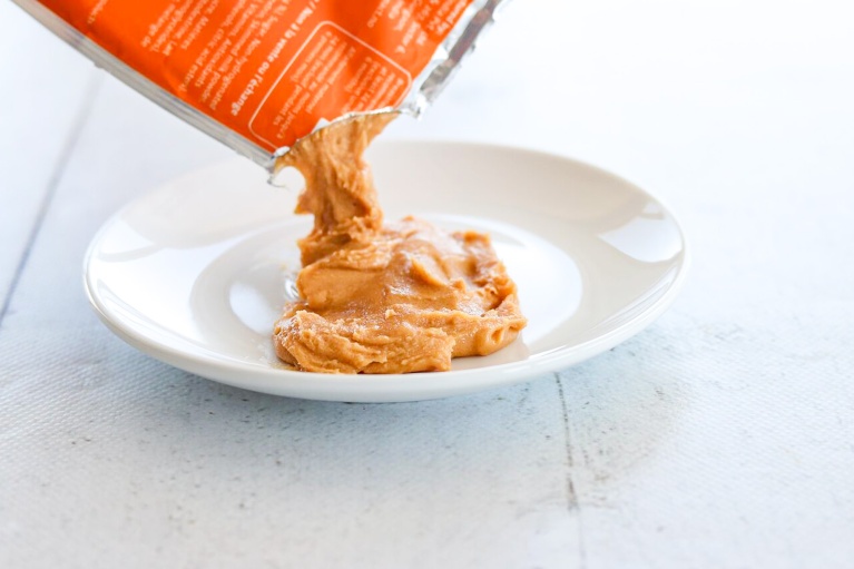 Weiße Schale mit Erdnusspaste auf weißem Holzhintergrund.